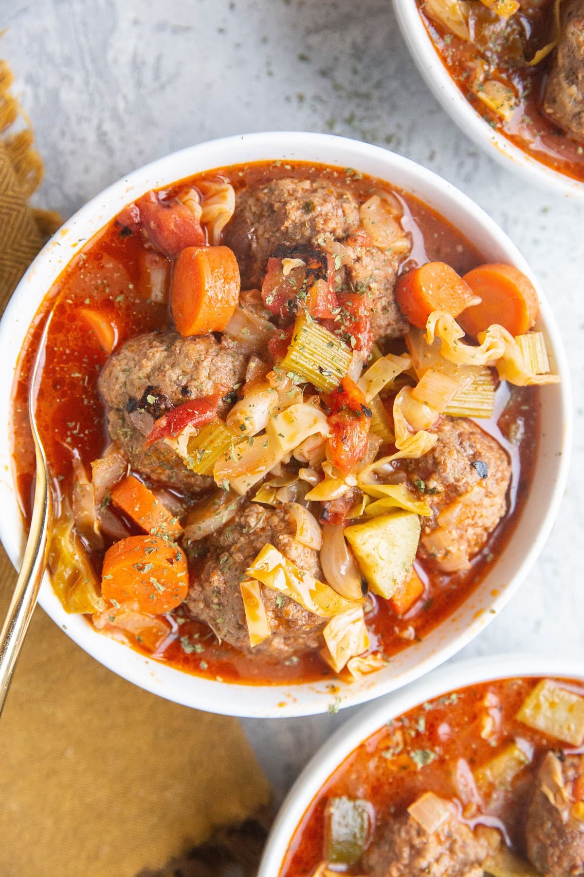 three white bowls of meatball soup with vegetables.