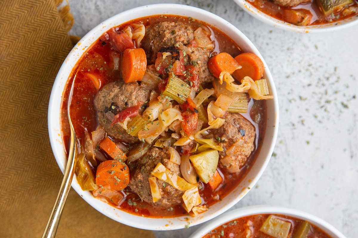 Horizontal photo of three white bowls of Sicilian Meatball Soup with Cabbage on a light background, ready to be served.