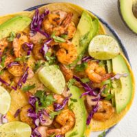 top down image of plate of shrimp tacos with avocado, cabbage and chipotle sauce