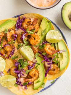 top down image of plate of shrimp tacos with avocado, cabbage and chipotle sauce