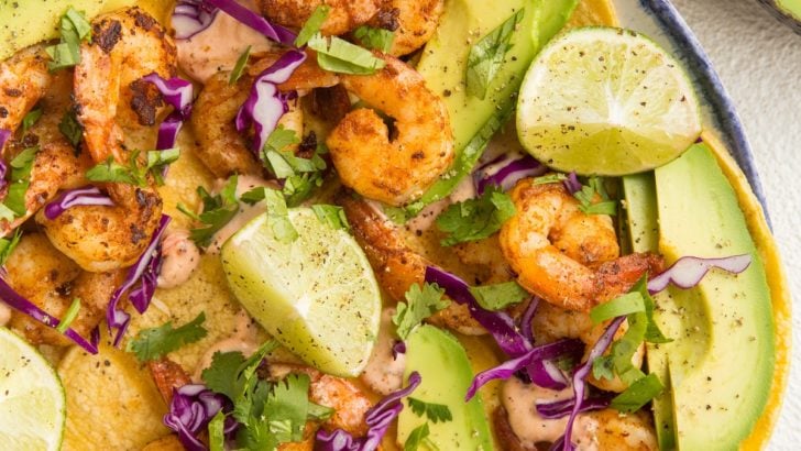 top down image of plate of shrimp tacos with avocado, cabbage and chipotle sauce