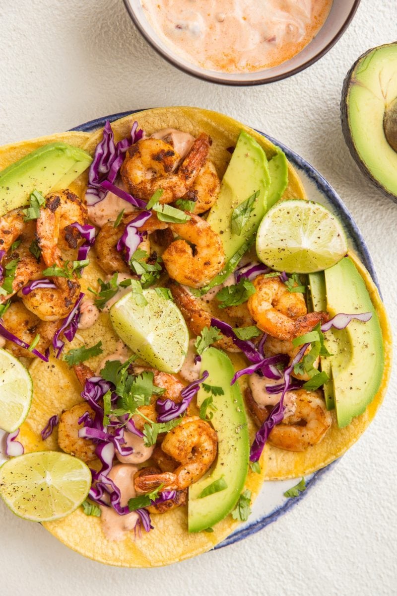 top down image of plate of shrimp tacos with avocado, cabbage and chipotle sauce