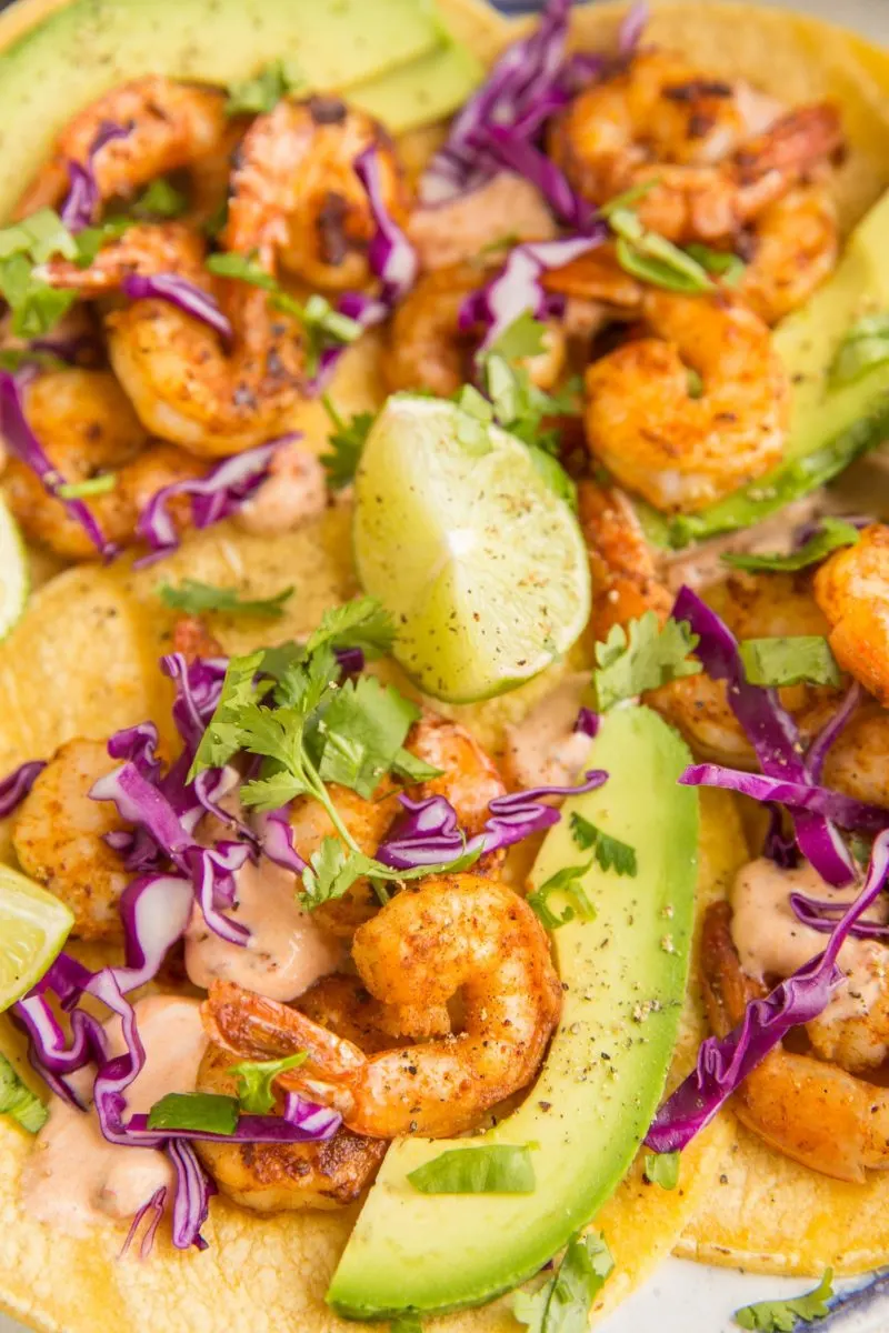 Close up image of shrimp tacos with slices of avocado, limes, and red cabbage