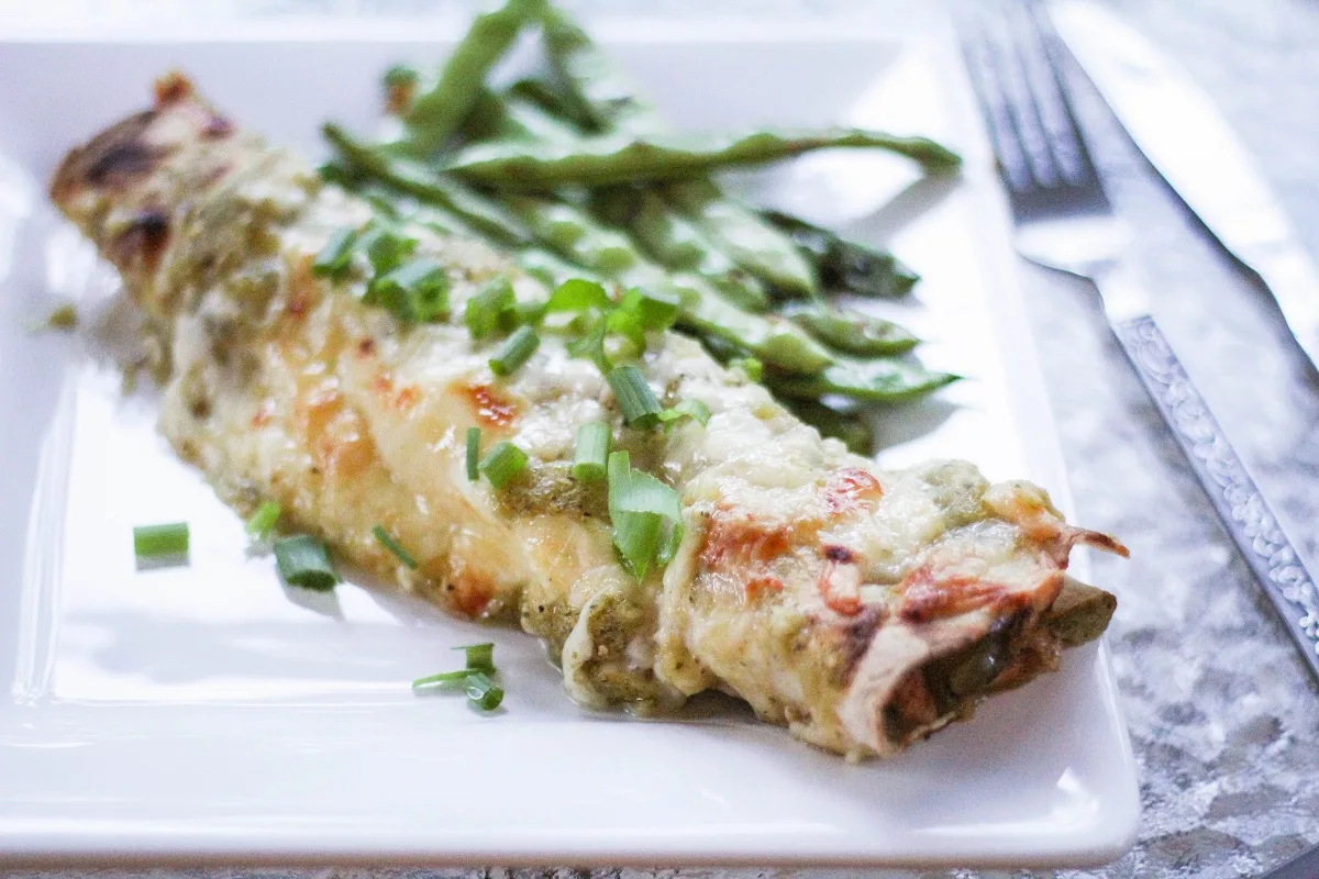 One green enchilada on a square white plate, served with green beans.