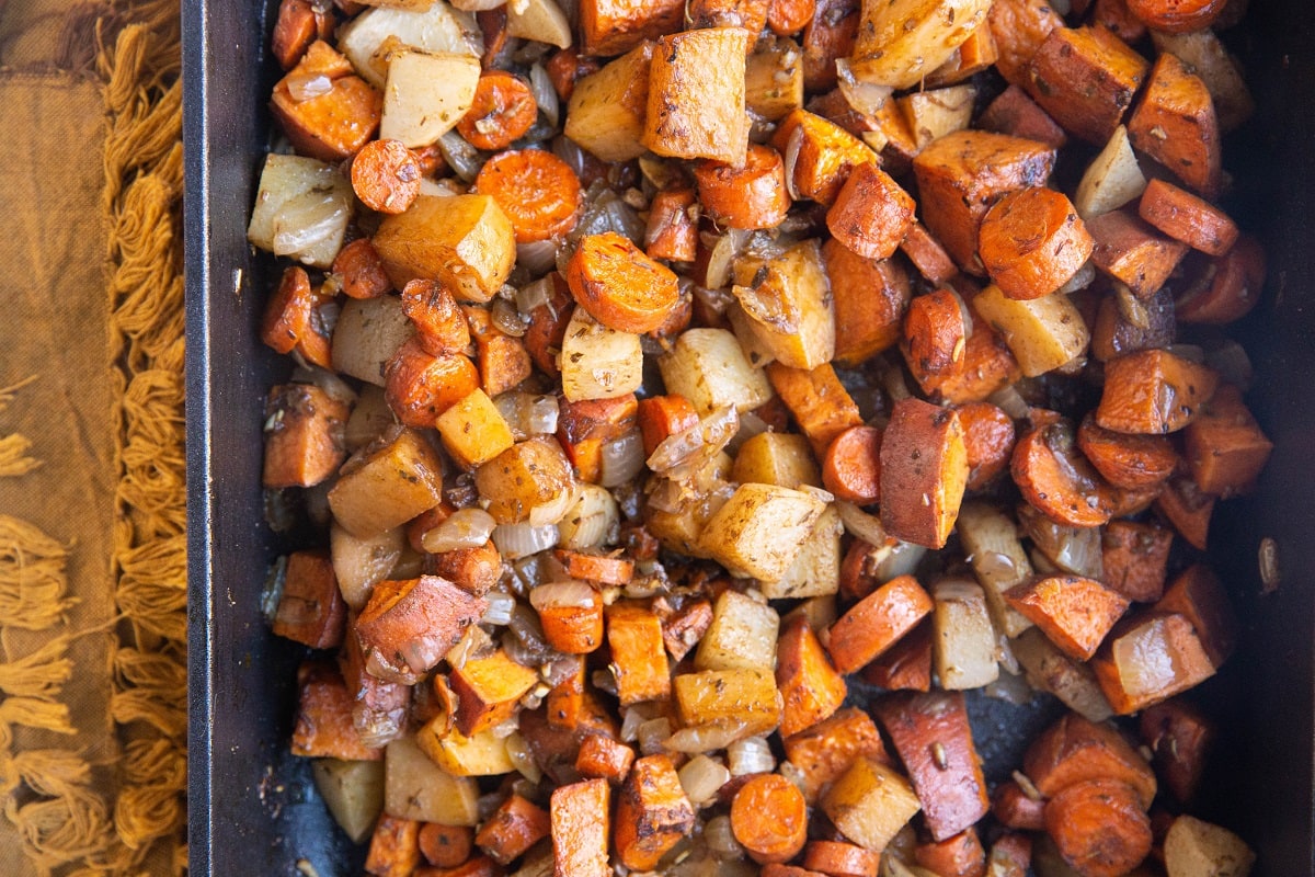 Balsamic Roasted Root Vegetables in a large casserole dish with a golden napkin to the side. Fresh out of the oven, ready to serve