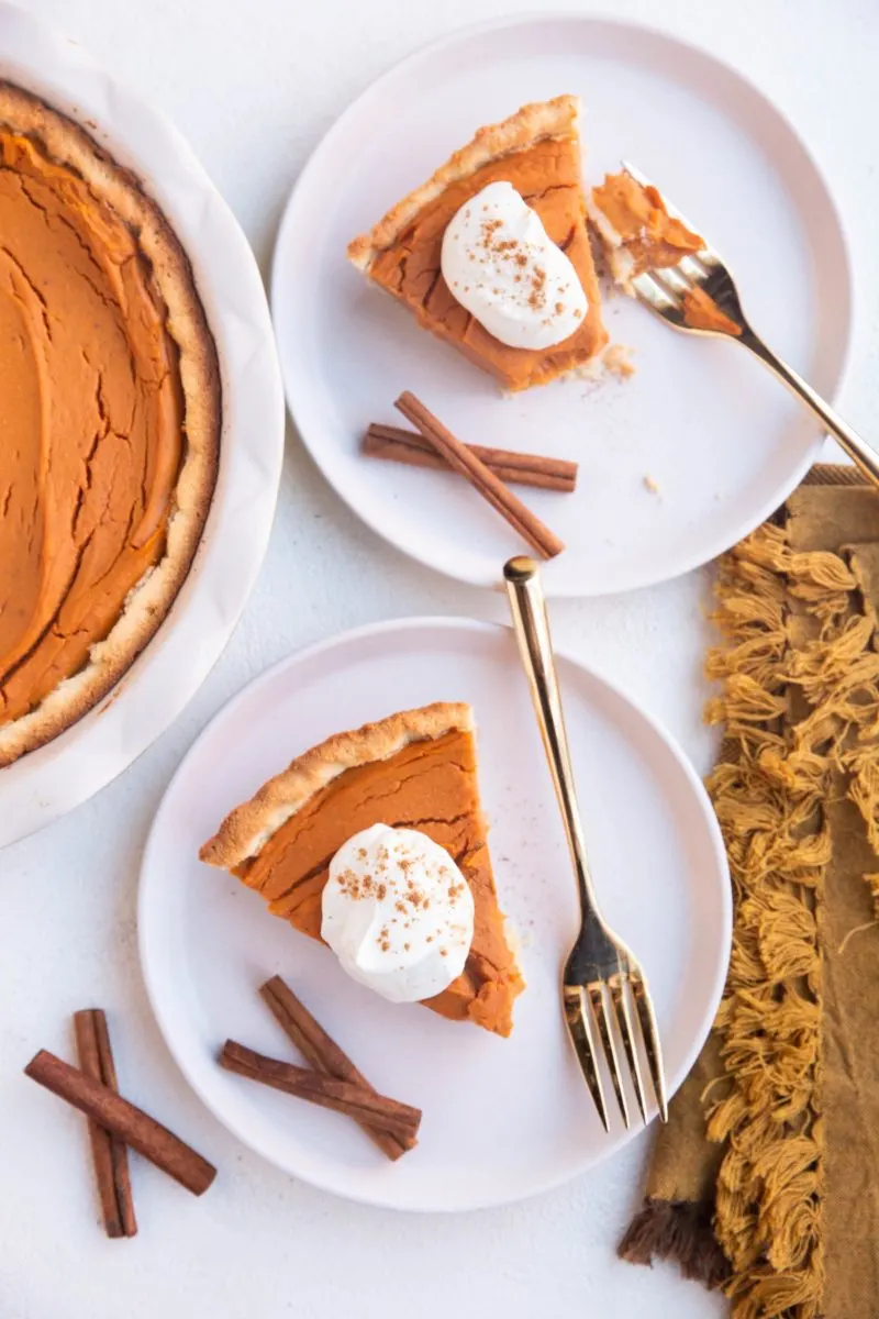 Top down photo of two white plates with slices of sweet potato pie with whipped cream on top and gold forks.
