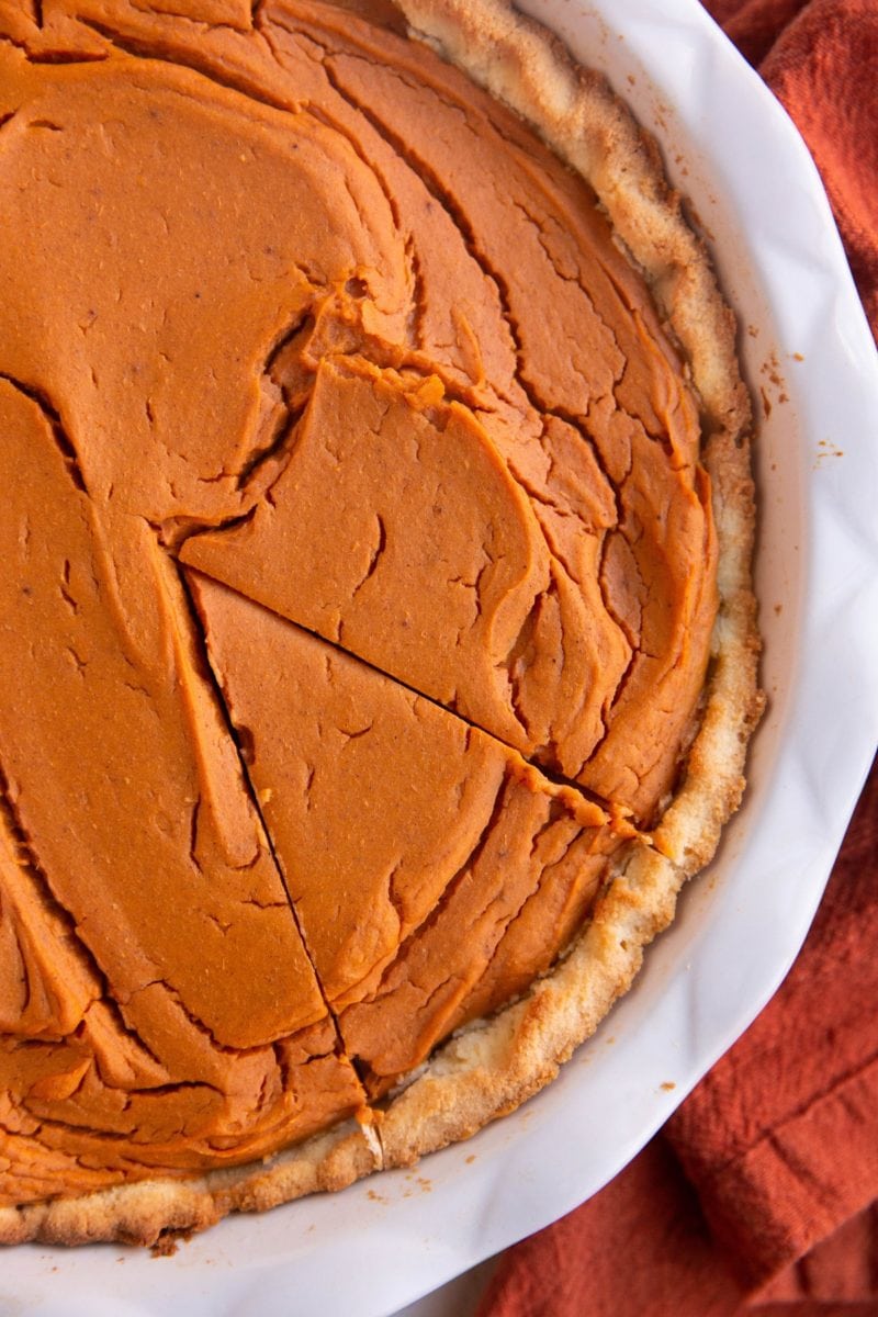 Whole sweet potato pie in a pie dish with one slice carved out.