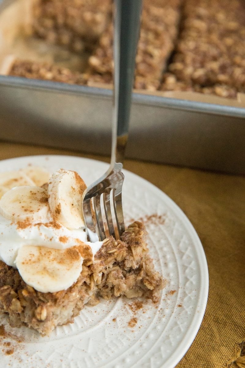 White plate with a slice of baked oatmeal with yogurt on top and banana slices