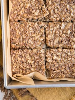 Horizontal photo of banana baked oatmeal in a baking pan sliced into squares with a bunch of bananas off to the side