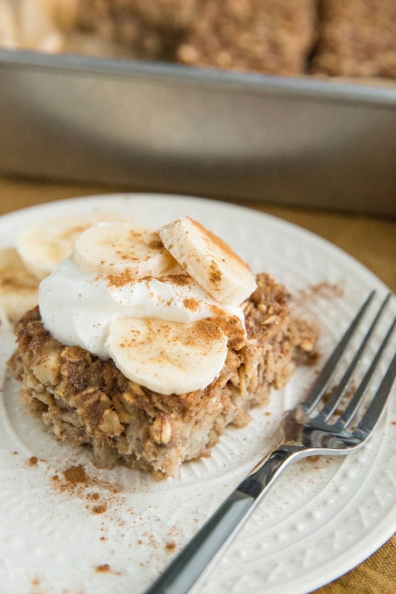 Slice of banana baked oatmeal on a plate with yogurt on top and slices of banana