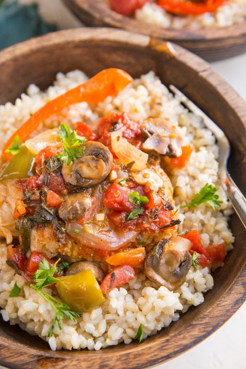 Wooden bowl with brown rice and chicken cacciatore with green bell peppers, tomatoes and onions and fresh parsley on top