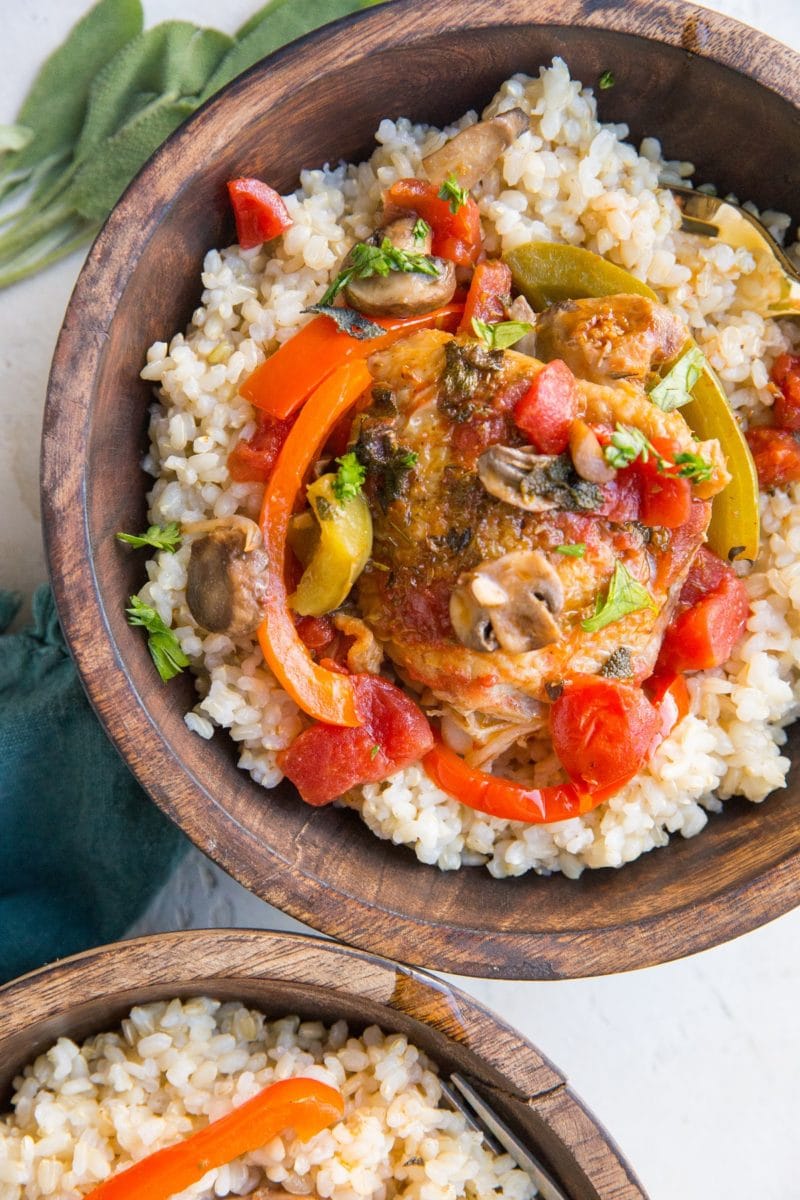 Two wooden bowls with rice and chicken cacciatore with red bell pepper, mushrooms, onion, and tomato sauce