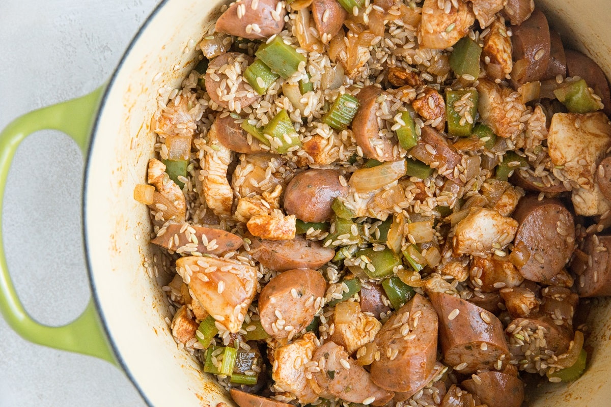 Process shot of making jambalaya with sautéed vegetables, chicken, sausage and rice in a large pot with seasonings