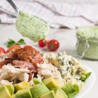 Cobb Salad with Homemade Green Goddess Dressing in a white bowl with green goddess dressing in the background on a marble surface.