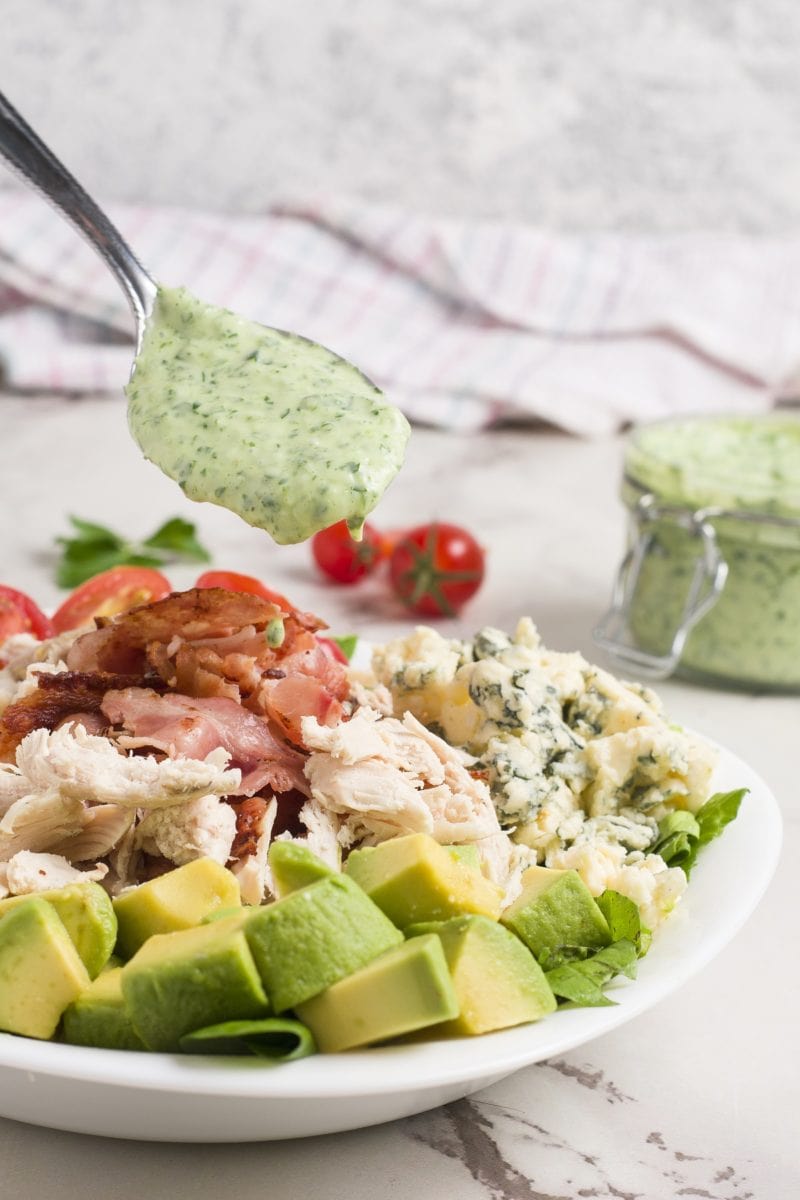 Cobb Salad with Homemade Green Goddess Dressing in a white bowl with green goddess dressing in the background on a marble surface.
