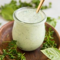 Mayo-Free Green Goddess Dressing in a small wreck jar with fresh basil and fresh parsley to the side