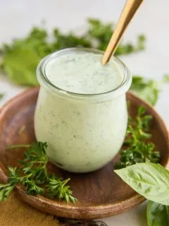 Mayo-Free Green Goddess Dressing in a small wreck jar with fresh basil and fresh parsley to the side