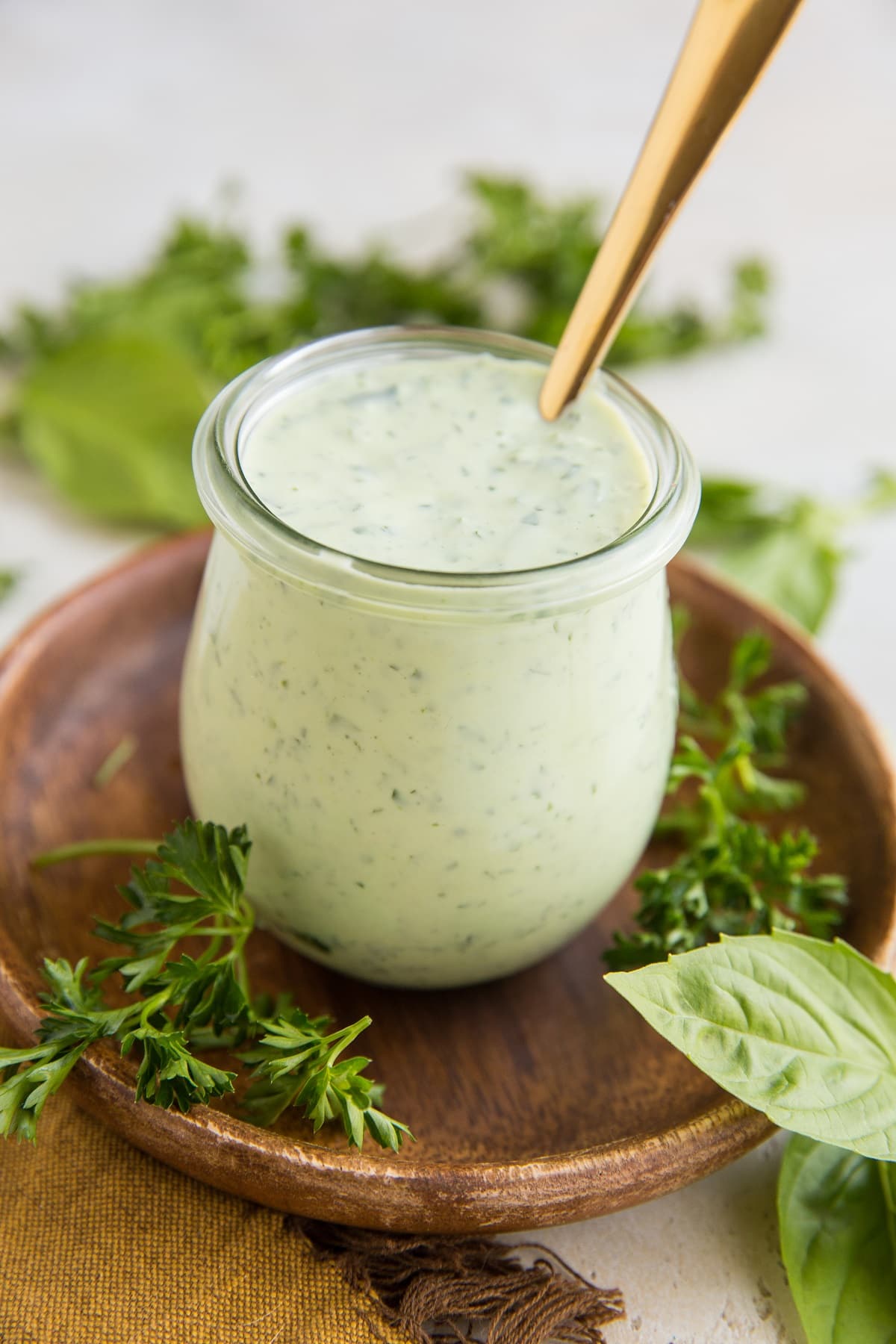 Mayo-Free Green Goddess Dressing in a small wreck jar with fresh basil and fresh parsley to the side