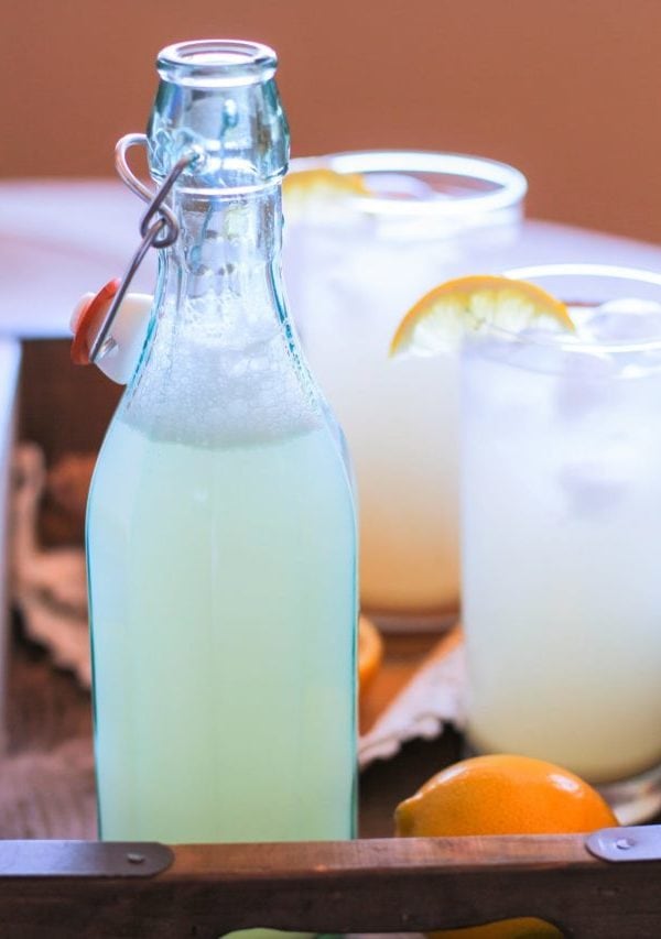 A bottle and two glasses of ginger beer inside of a serving tray with a lemon.