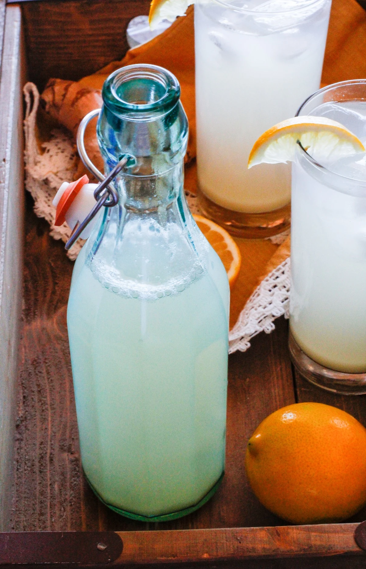 Wooden serving tray with one bottle and two glasses of ginger beer.