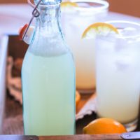 A bottle and two glasses of ginger beer inside of a serving tray with a lemon.
