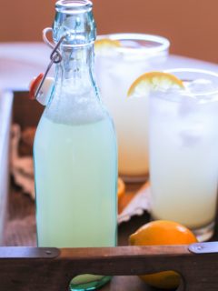 A bottle and two glasses of ginger beer inside of a serving tray with a lemon.