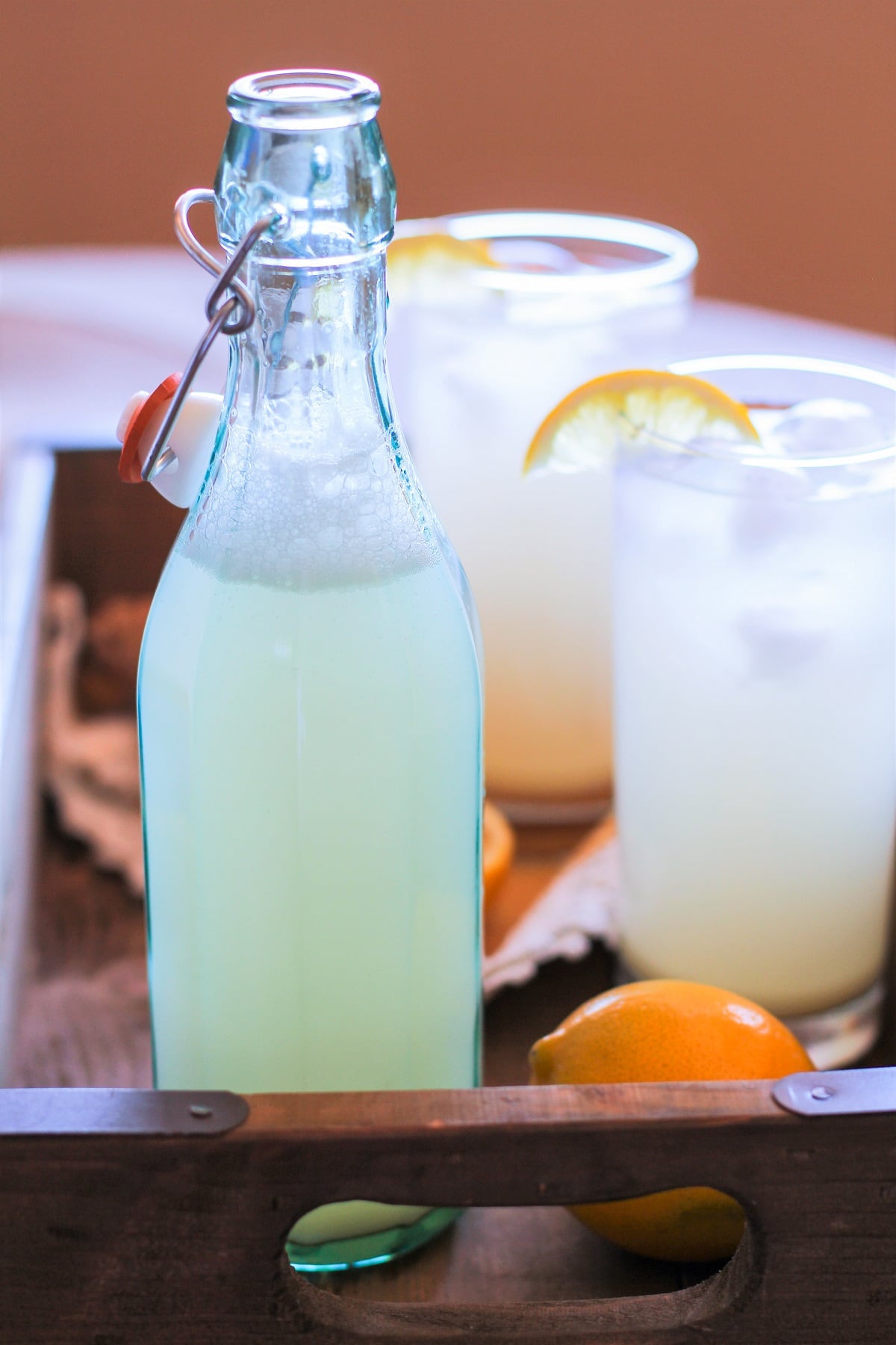 A bottle and two glasses of ginger beer inside of a serving tray with a lemon.