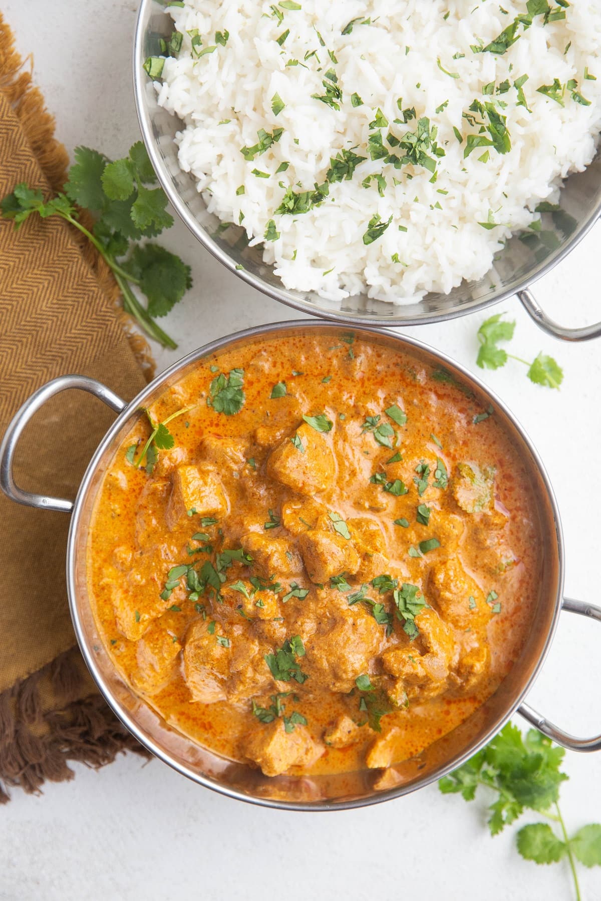 metal Indian dish of chicken tikka masala and a separate dish of steamed white rice. Fresh cilantro all around.