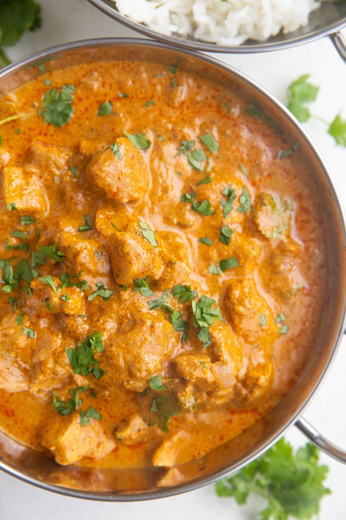 Top down image of a serving dish of chicken tikka masala sprinkled with fresh cilantro and a serving dish of jasmine rice.