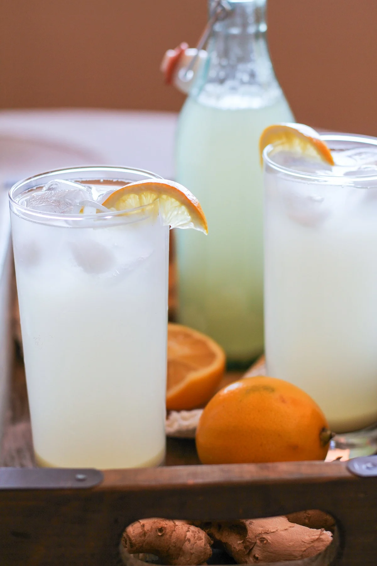 Two full glasses of ginger soda with lemon slices and a bottle in the background
