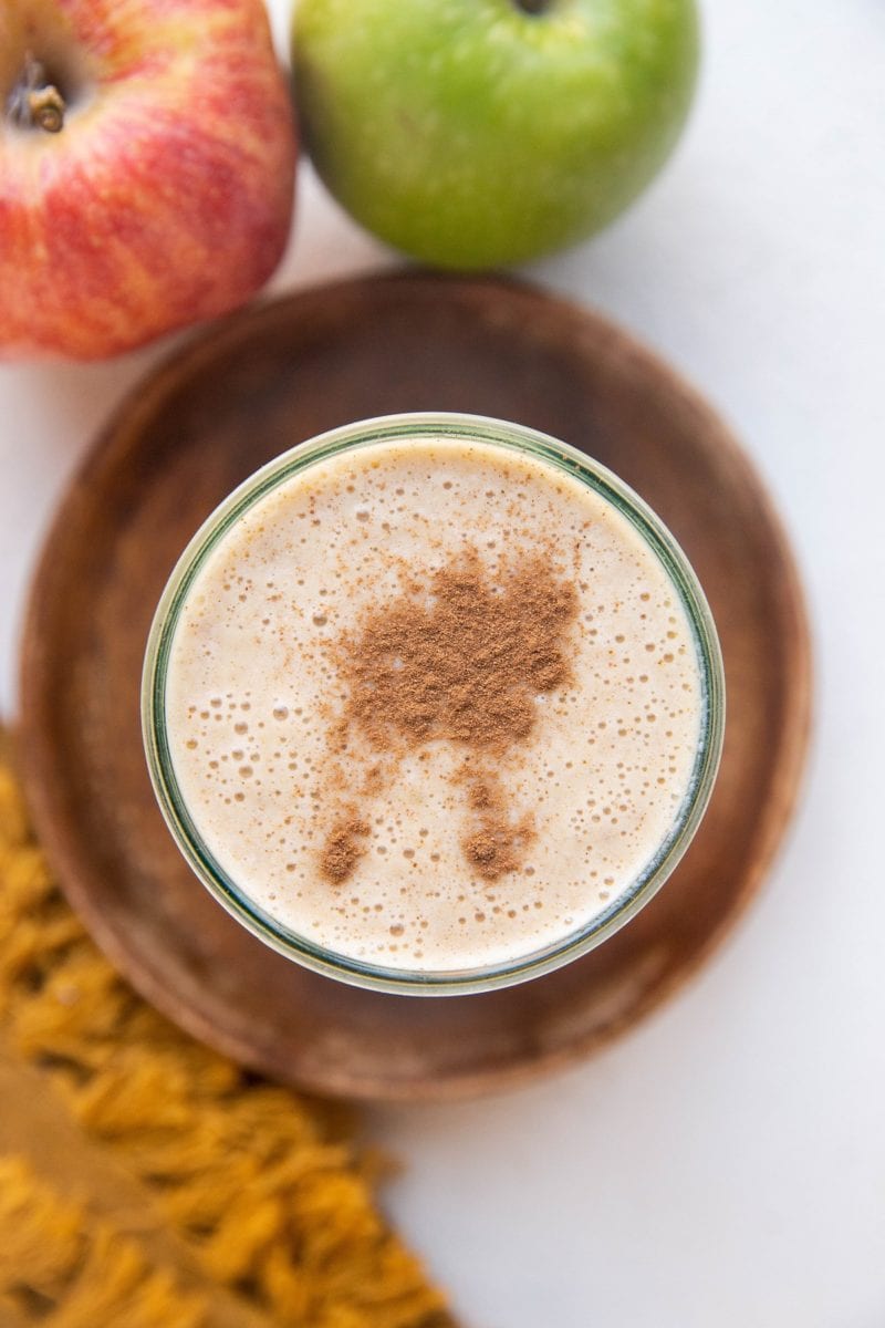 Top down image of an Apple Pie Almond Butter Smoothie in a glass with fresh apples to the side.