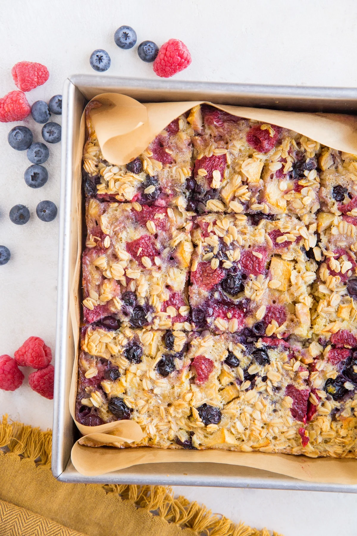 baking pan with finished baked oatmeal sliced into bars with berries all around