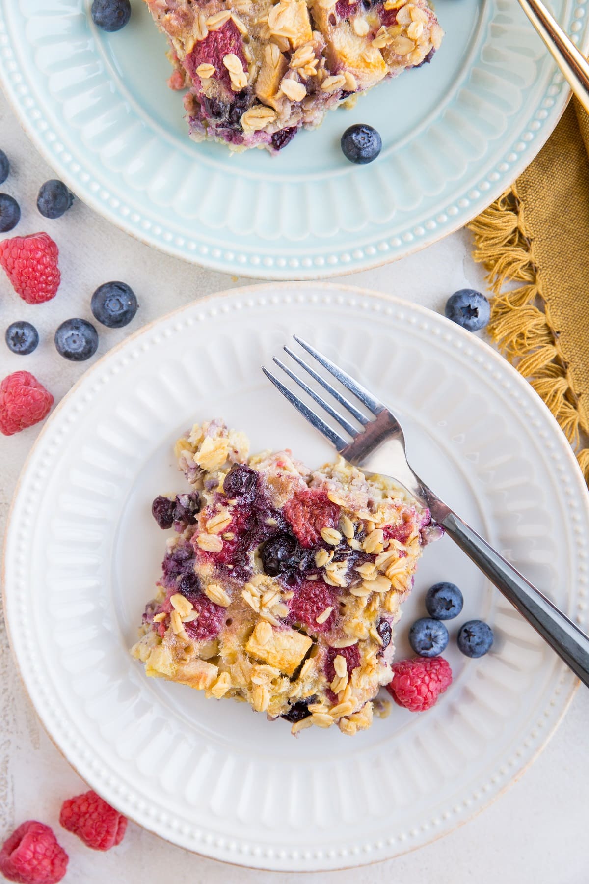 Two plates of Mixed Berry and Apple Baked Oatmeal top down with fresh berries all around