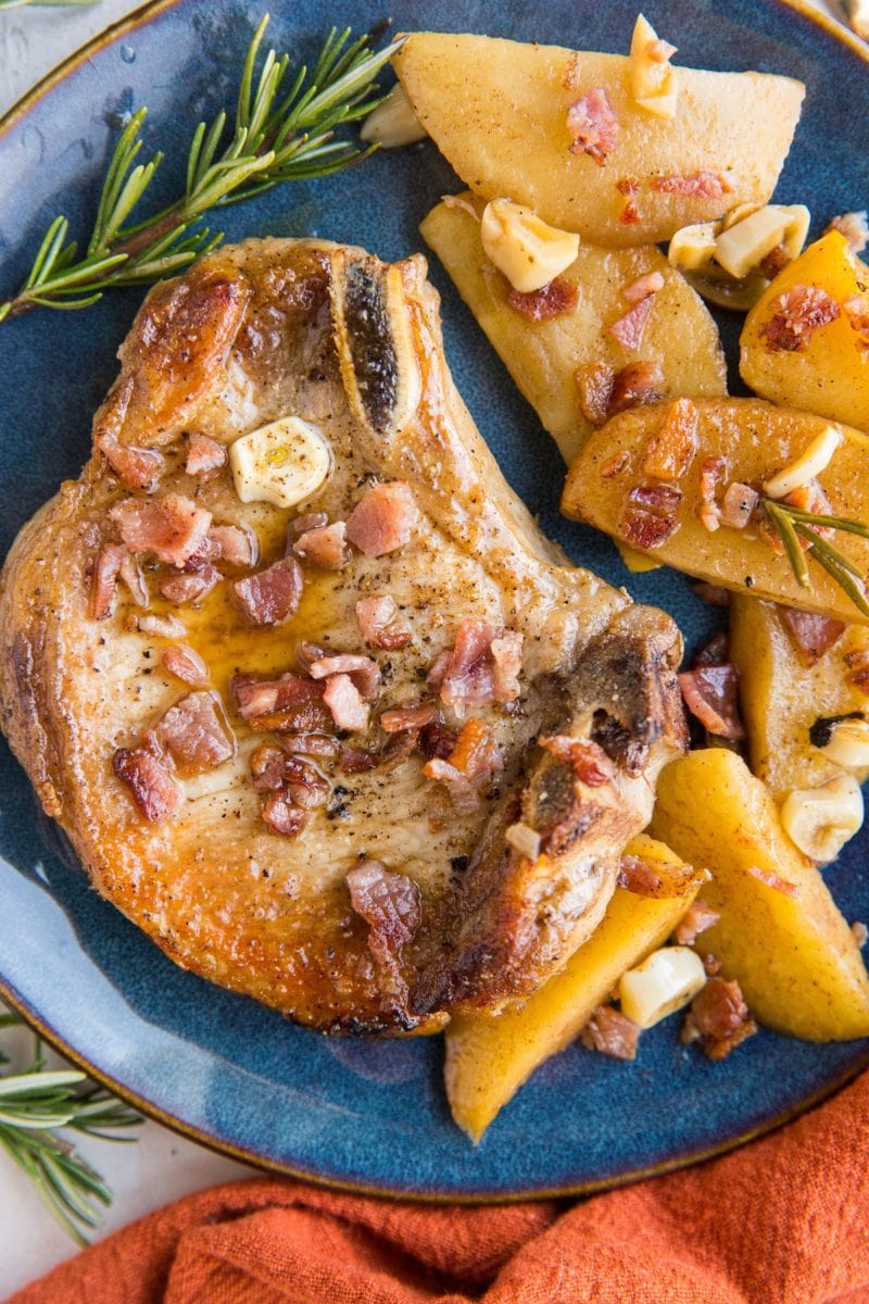 Roasted pork chop on a blue plate with stewed apples on the side and a red napkin with fresh rosemary