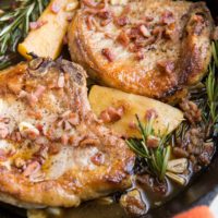 Roasted pork chops in a cast iron skillet with a red napkin around the handle