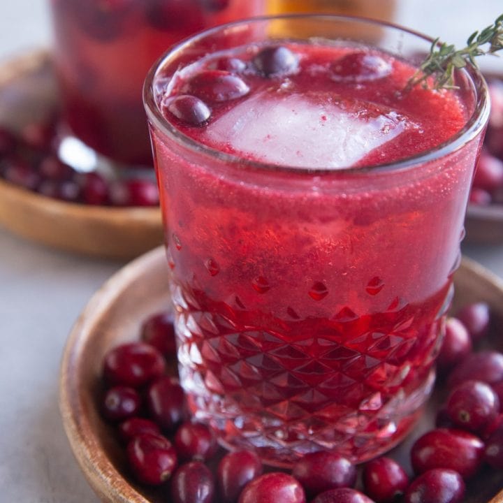 Close up image of a cranberry cocktail sitting on a wooden plate with fresh cranberries all around