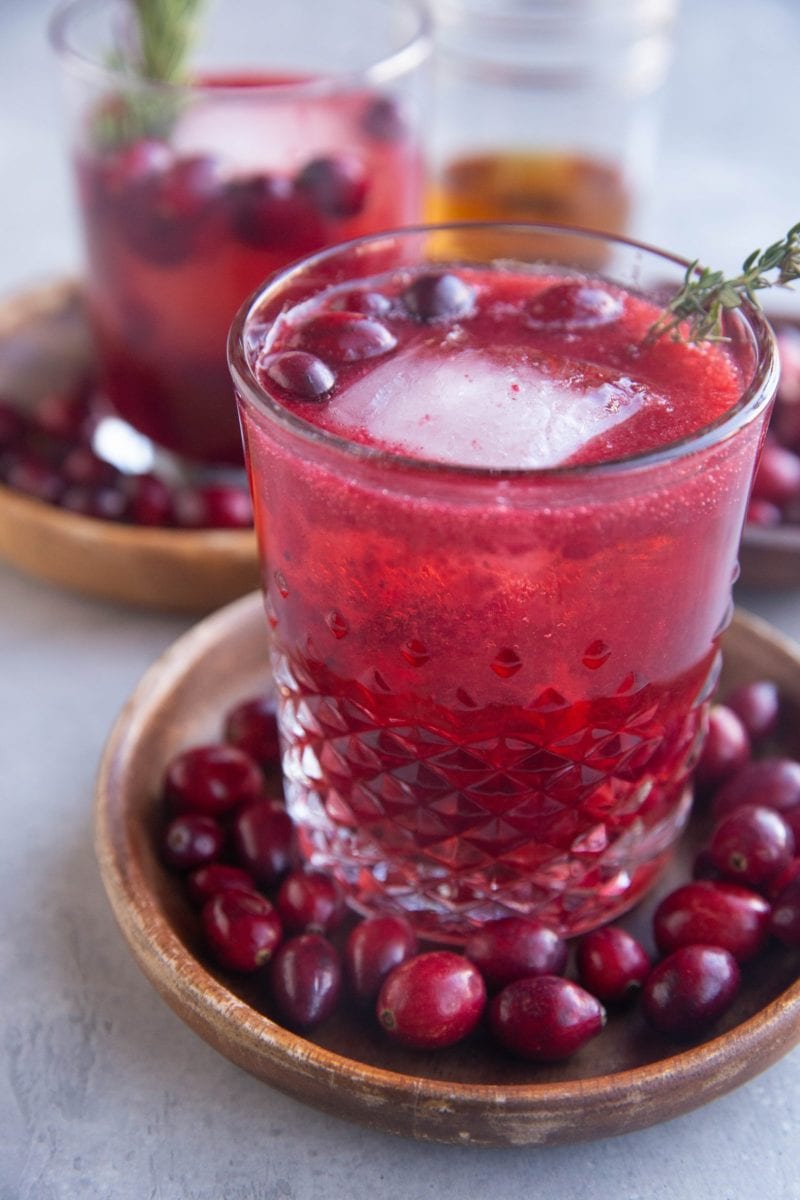 Close up image of a cranberry cocktail sitting on a wooden plate with fresh cranberries all around