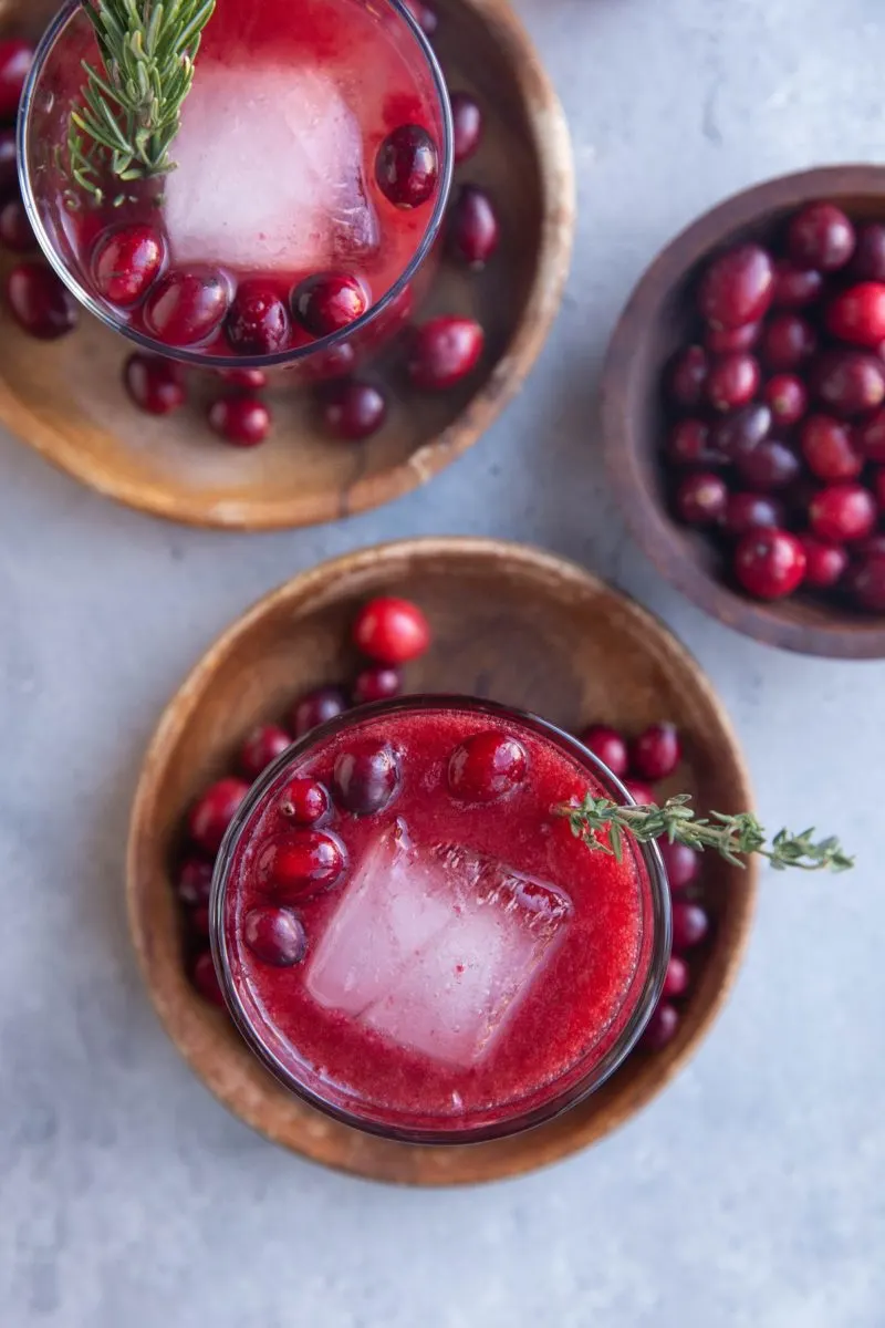 Two glasses of cranberry cocktails on wooden plates.