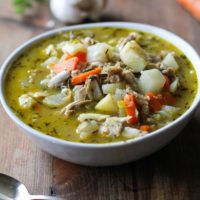 Big bowl of turkey soup with root vegetables with vegetables in the background