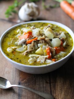 Big bowl of turkey soup with root vegetables with vegetables in the background