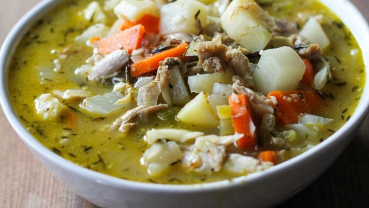 Big bowl of turkey soup with root vegetables with vegetables in the background