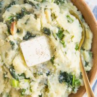 Close up image of colcannon in a wooden bowl with a blue striped napkin, a gold spoon and melted butter on top of the potatoes