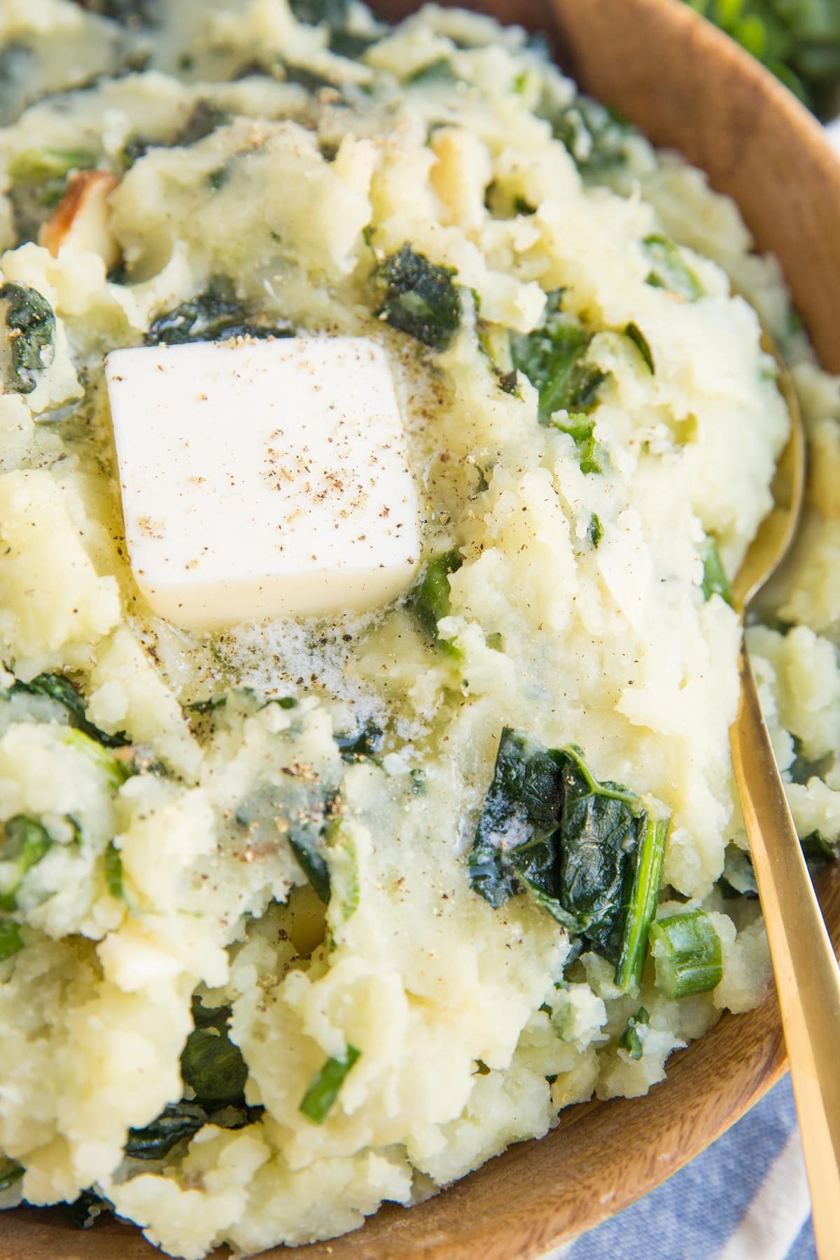 Colcannon mashed potatoes in a wooden bowl with a pat of melted butter on top and a gold spoon