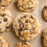 Cookie sheet with 7 large almond flour chocolate chip cookies and walnut halves next to cookies