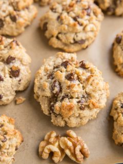 Cookie sheet with 7 large almond flour chocolate chip cookies and walnut halves next to cookies