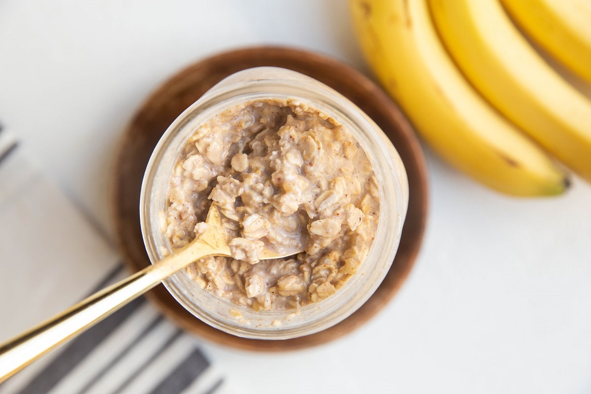 Jar of banana bread oatmeal with a gold spoon taking a scoop.