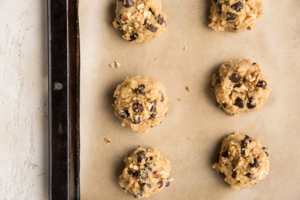 Baking sheet lined with parchment paper with mounds of cookie dough ready to go into the oven