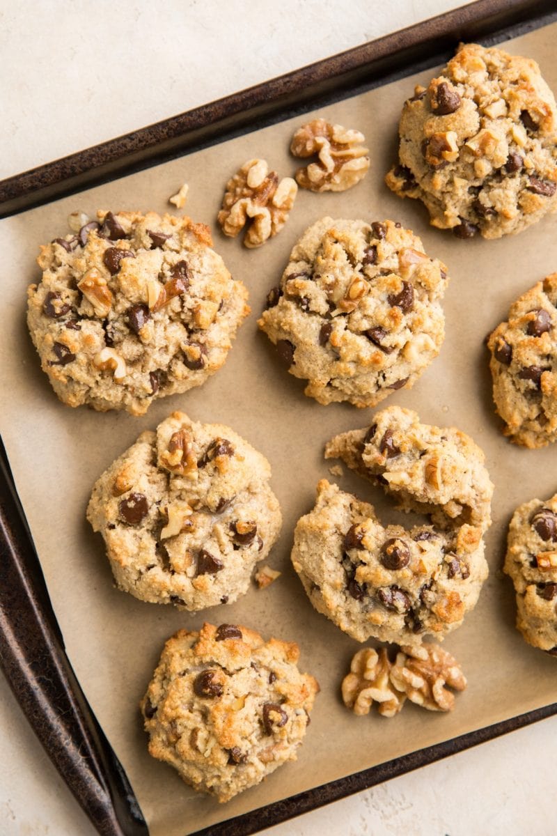 Cookie sheet with grain-free chocolate chip cookies on it on top of parchment paper with a few walnuts next to the cookies