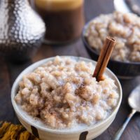 Two bowls of dairy-free rice pudding with a candle in the background and a spoon and golden napkin to the side.