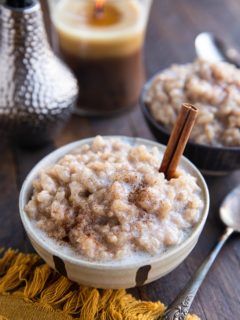 Two bowls of dairy-free rice pudding with a candle in the background and a spoon and golden napkin to the side.